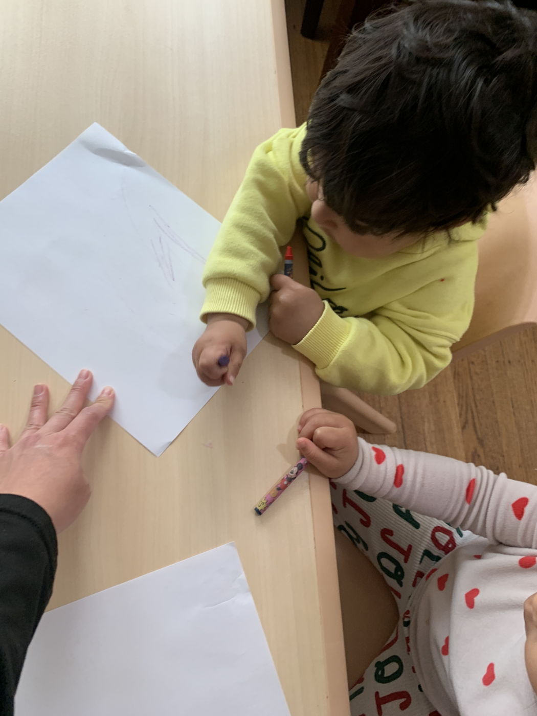 A toddler drawing on paper with a crayon